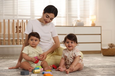 Photo of Mother with her cute little twins and toys on floor at home