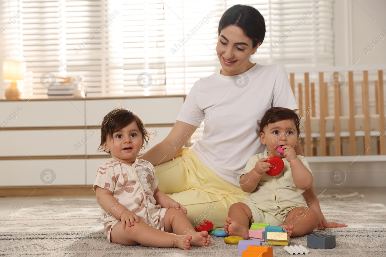Mother with her cute little twins and toys on floor at home Photo of Mother with her cute little twins and toys on floor at home