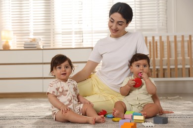 Photo of Mother with her cute little twins and toys on floor at home