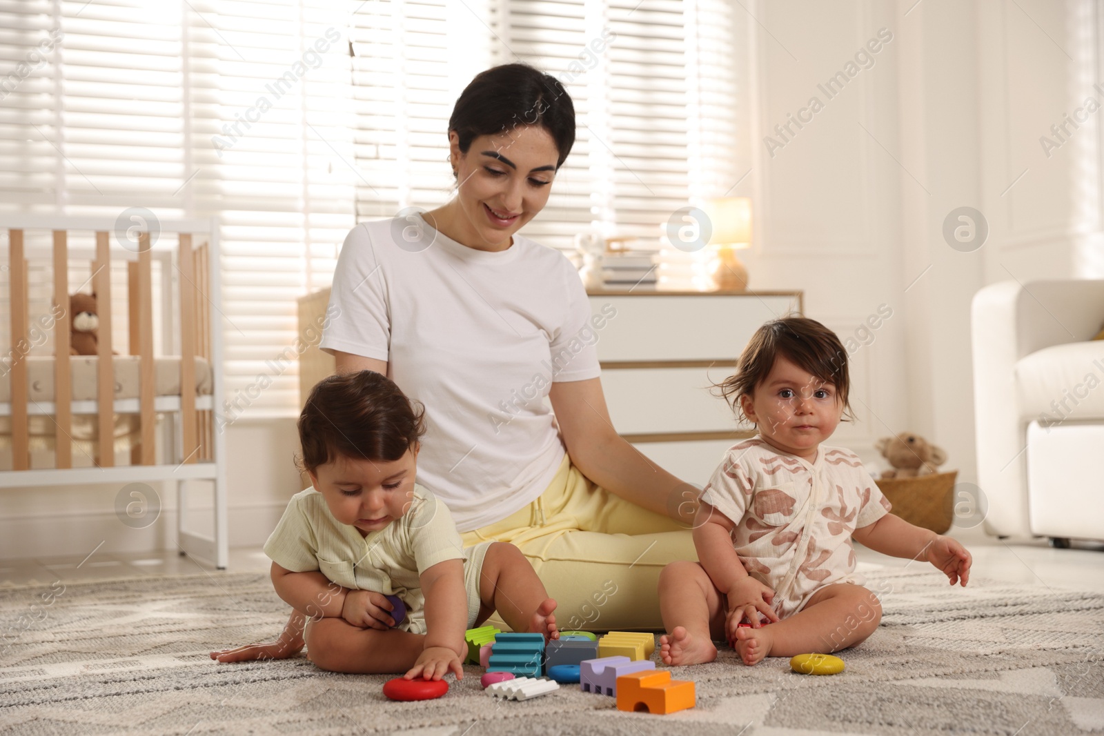 Mother with her cute little twins and toys on floor at home Photo of Mother with her cute little twins and toys on floor at home