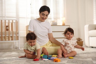 Photo of Mother with her cute little twins and toys on floor at home
