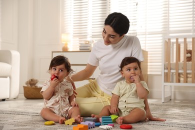 Photo of Mother with her cute little twins and toys on floor at home