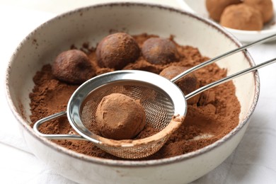 Photo of Making tasty chocolate candies with cocoa powder at light table, closeup