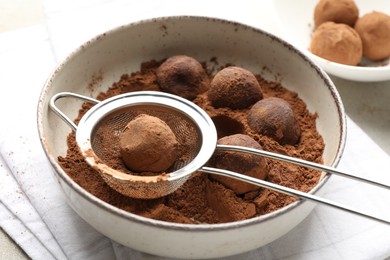 Photo of Making tasty chocolate candies with cocoa powder at light table, closeup
