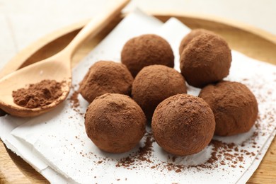 Photo of Tasty chocolate candies with cocoa powder and spoon on light table, closeup