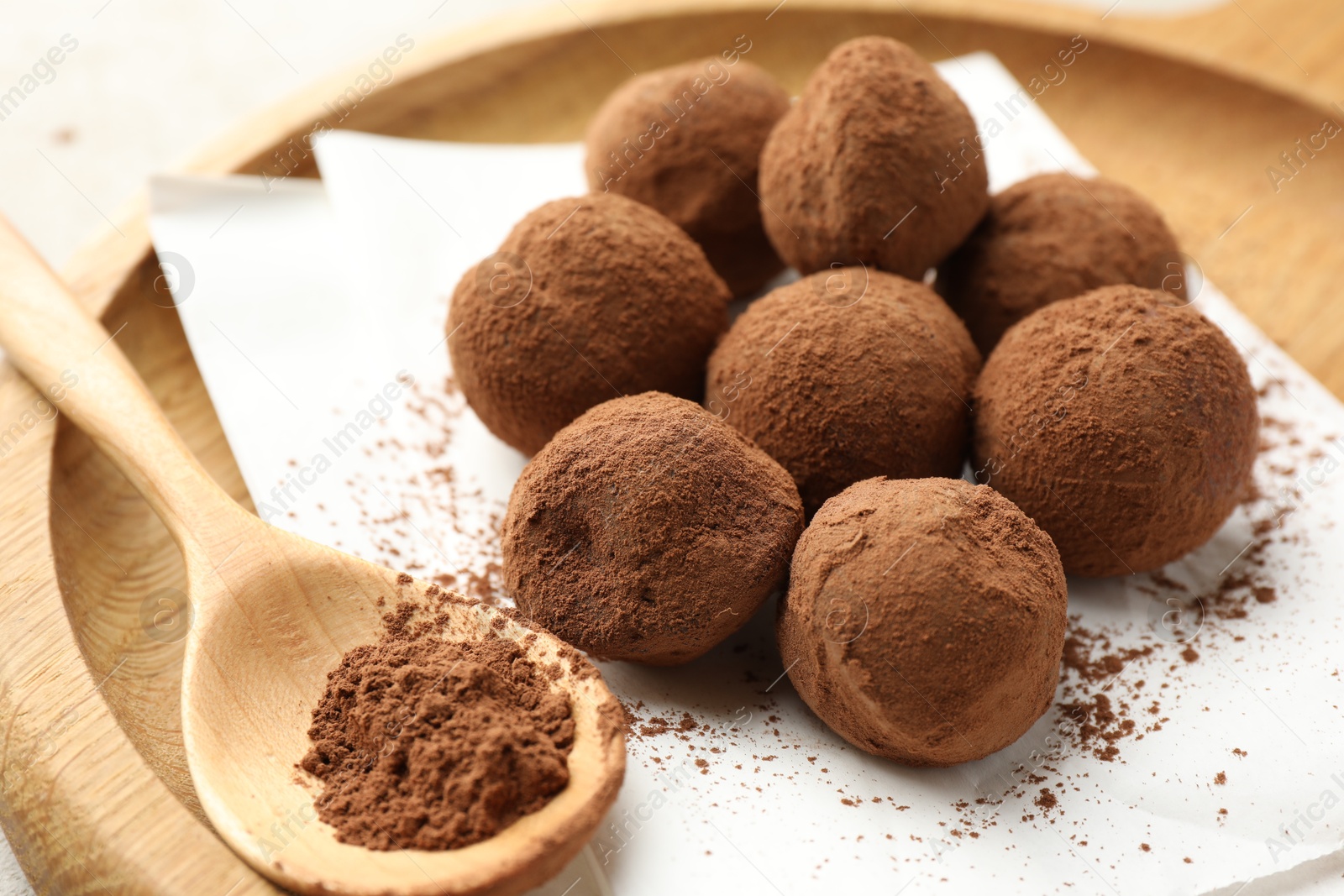 Tasty chocolate candies with cocoa powder and spoon on light table, closeup Photo of Tasty chocolate candies with cocoa powder and spoon on light table, closeup