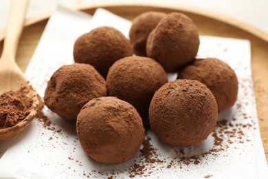 Photo of Tasty chocolate candies with cocoa powder and spoon on light table, closeup
