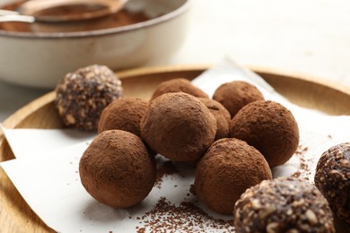 Photo of Tasty chocolate candies with cocoa powder on light table, closeup