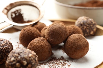 Photo of Tasty chocolate candies with cocoa powder and strainer on light table, closeup