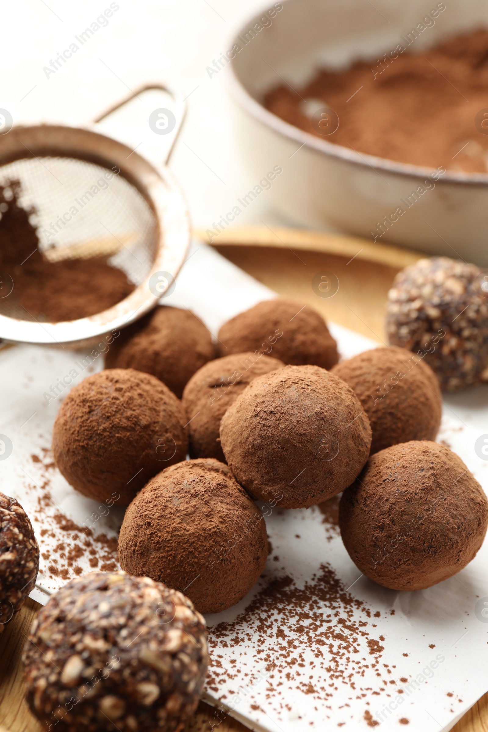 Tasty chocolate candies with cocoa powder and strainer on light table, closeup Photo of Tasty chocolate candies with cocoa powder and strainer on light table, closeup