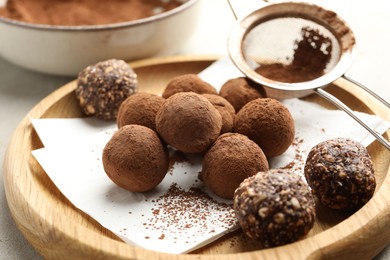 Photo of Tasty chocolate candies with cocoa powder and strainer on light table, closeup