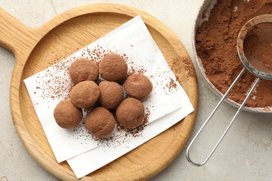 Photo of Tasty chocolate candies with cocoa powder and strainer on light table, flat lay
