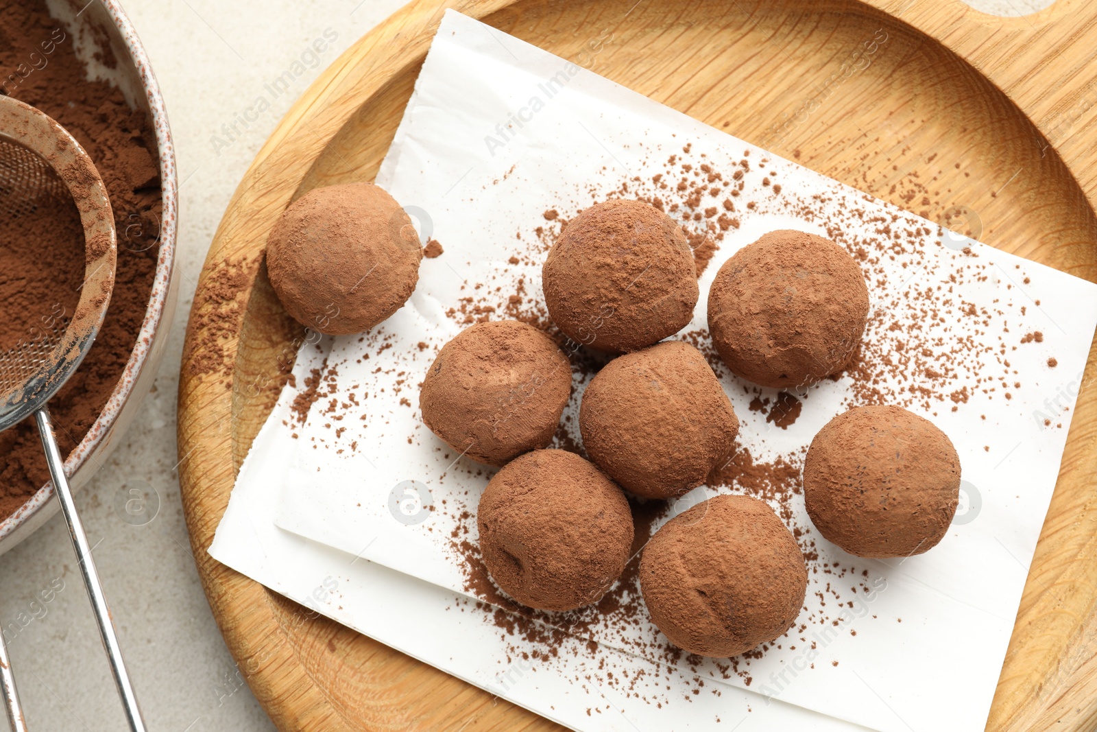 Tasty chocolate candies with cocoa powder and strainer on light table, flat lay Photo of Tasty chocolate candies with cocoa powder and strainer on light table, flat lay
