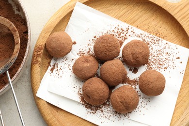 Photo of Tasty chocolate candies with cocoa powder and strainer on light table, flat lay