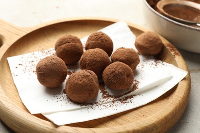Photo of Tasty chocolate candies with cocoa powder on light table, closeup