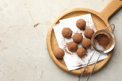 Photo of Tasty chocolate candies with cocoa powder and strainer on light table, top view. Space for text