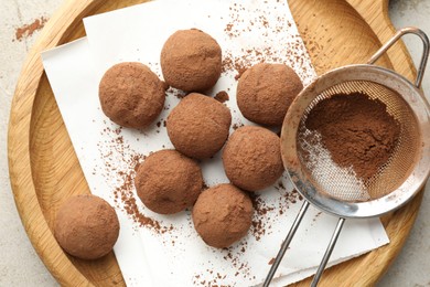 Photo of Tasty chocolate candies with cocoa powder and strainer on light table, top view