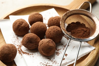 Photo of Tasty chocolate candies with cocoa powder and strainer on light table, closeup