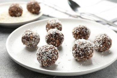 Photo of Tasty chocolate candies with nuts and coconut flakes on grey table, closeup