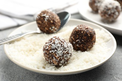 Photo of Making tasty chocolate candies with coconut flakes at grey table, closeup