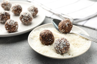 Photo of Making tasty chocolate candies with coconut flakes at grey table, closeup