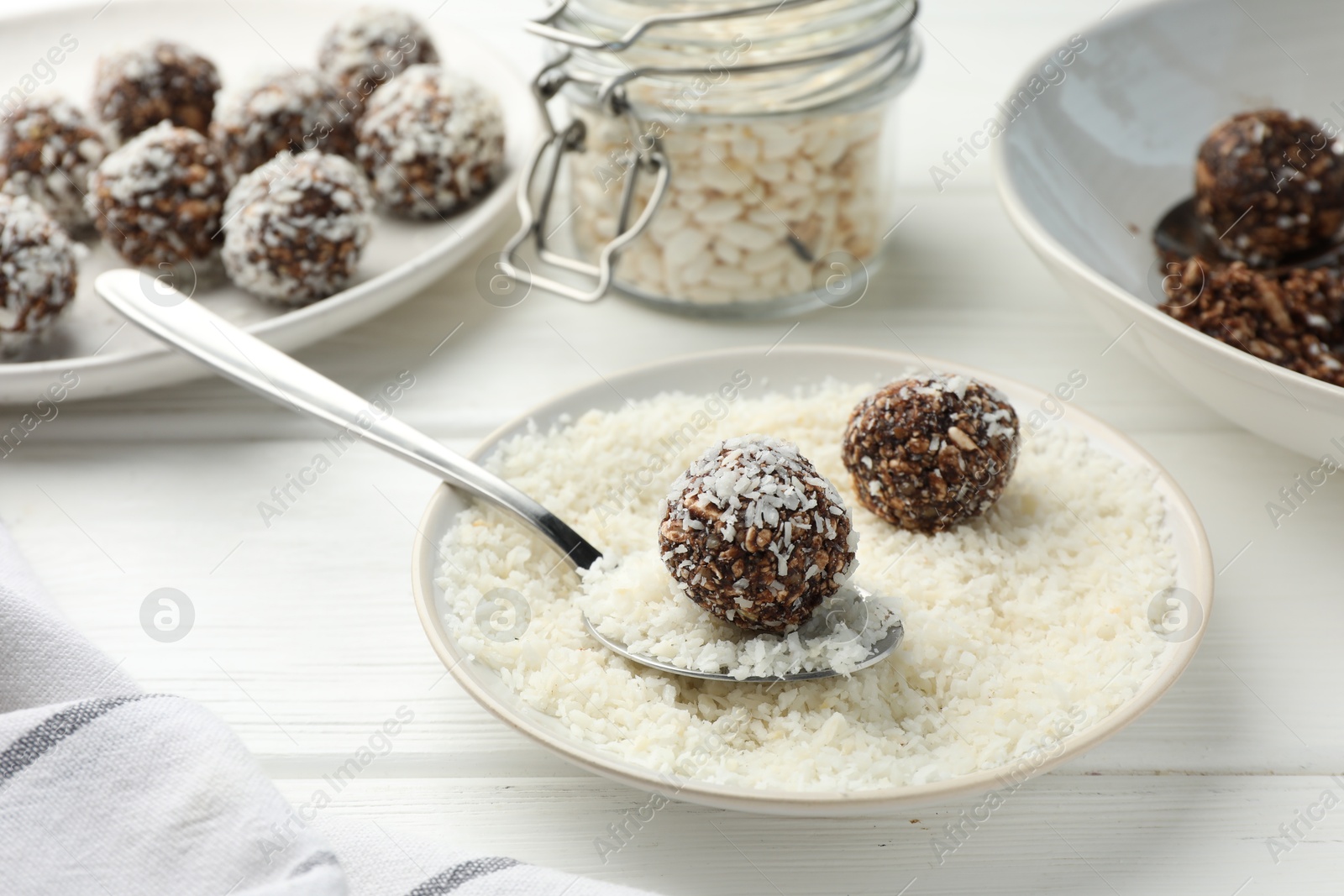 Tasty chocolate candies with nuts, coconut flakes and puffed rice on white wooden table, closeup Photo of Tasty chocolate candies with nuts, coconut flakes and puffed rice on white wooden table, closeup