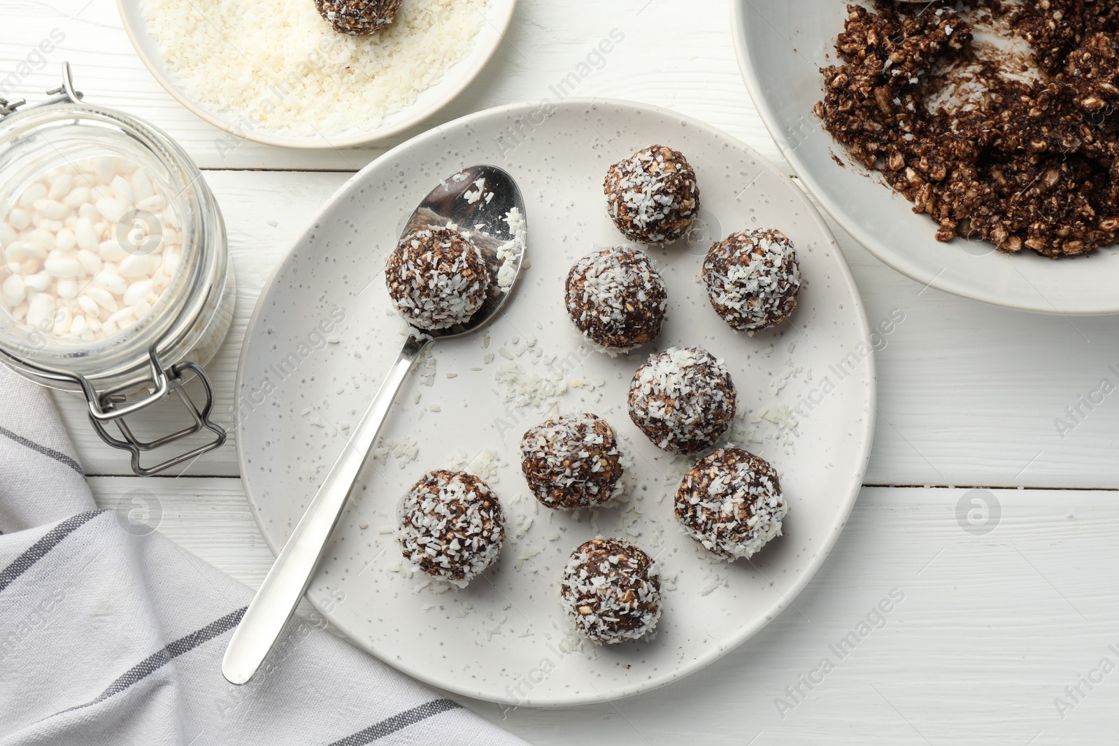 Tasty chocolate candies with nuts, coconut flakes and puffed rice on white wooden table, flat lay Photo of Tasty chocolate candies with nuts, coconut flakes and puffed rice on white wooden table, flat lay