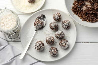Photo of Tasty chocolate candies with nuts, coconut flakes and puffed rice on white wooden table, flat lay