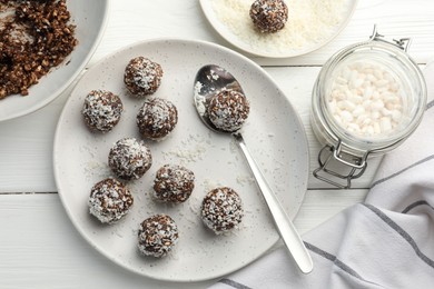 Photo of Tasty chocolate candies with nuts, coconut flakes and puffed rice on white wooden table, flat lay