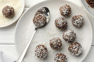 Photo of Tasty chocolate candies with nuts and coconut flakes on white wooden table, flat lay