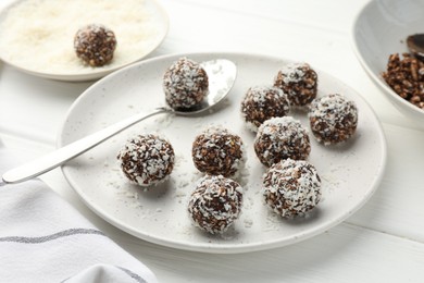 Photo of Tasty chocolate candies with nuts and coconut flakes on white wooden table, closeup
