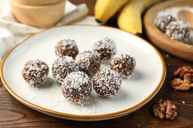 Photo of Tasty chocolate candies with nuts and coconut flakes on wooden table, closeup