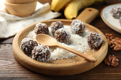 Photo of Tasty chocolate candies with nuts and coconut flakes on wooden table, closeup