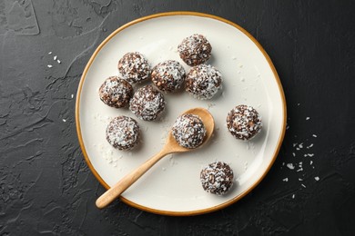 Photo of Tasty chocolate candies with nuts and coconut flakes on black table, top view