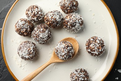 Photo of Tasty chocolate candies with nuts and coconut flakes on black table, top view