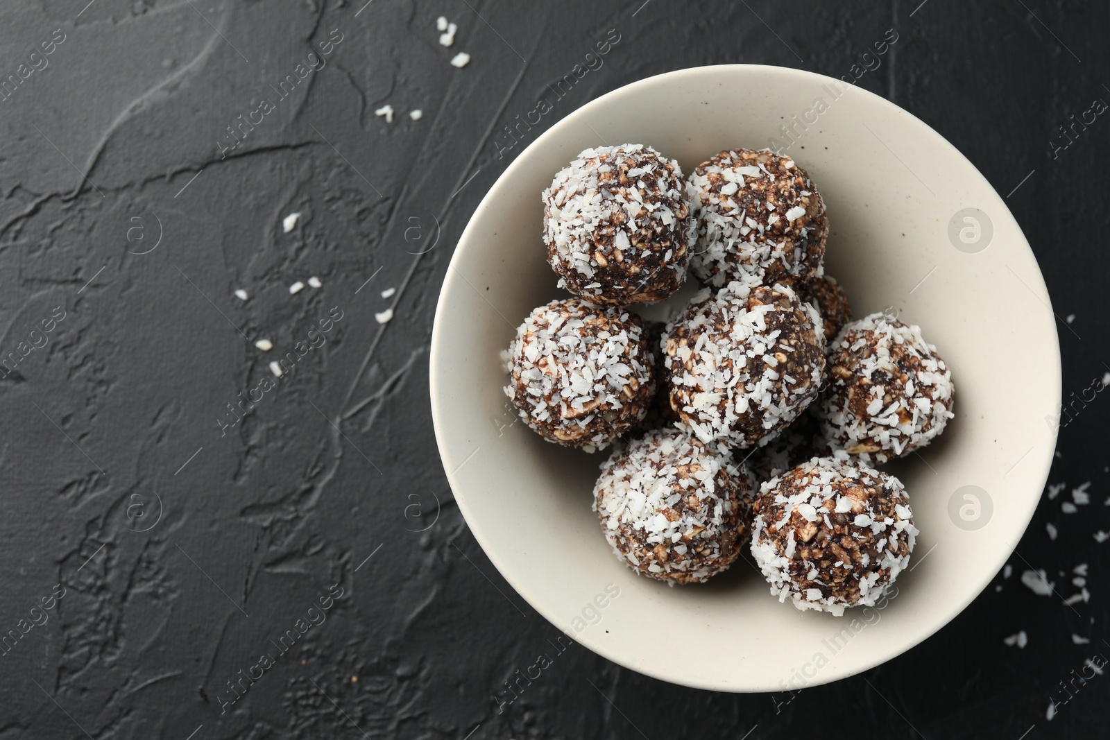 Tasty chocolate candies with nuts and coconut flakes in bowl on black table, top view. Space for text Photo of Tasty chocolate candies with nuts and coconut flakes in bowl on black table, top view. Space for text