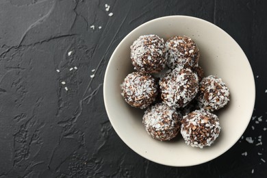 Photo of Tasty chocolate candies with nuts and coconut flakes in bowl on black table, top view. Space for text