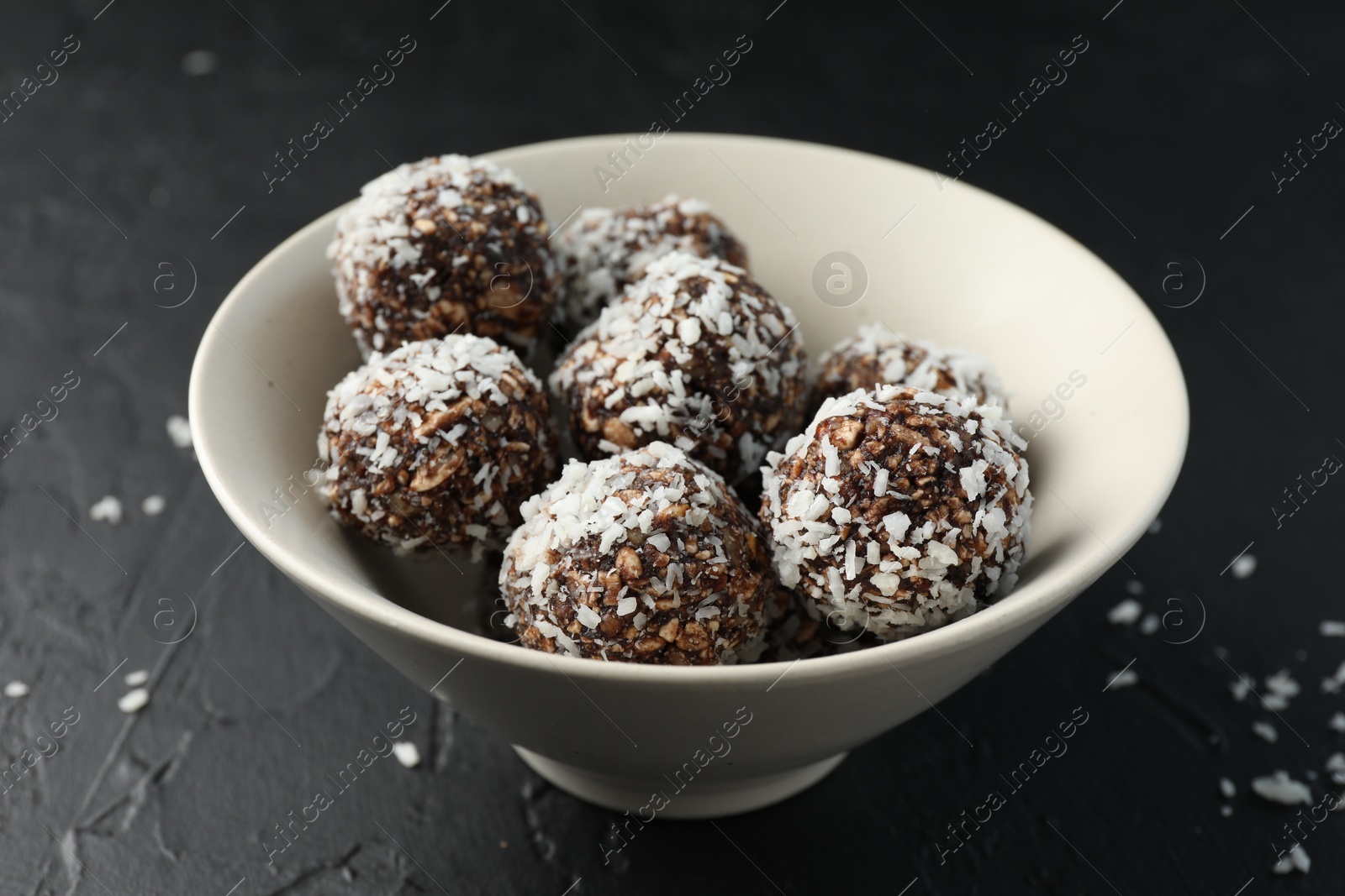 Tasty chocolate candies with nuts and coconut flakes in bowl on black table, closeup Photo of Tasty chocolate candies with nuts and coconut flakes in bowl on black table, closeup