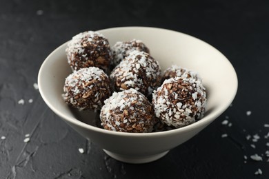 Photo of Tasty chocolate candies with nuts and coconut flakes in bowl on black table, closeup