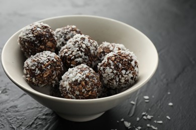 Photo of Tasty chocolate candies with nuts and coconut flakes in bowl on black table, closeup