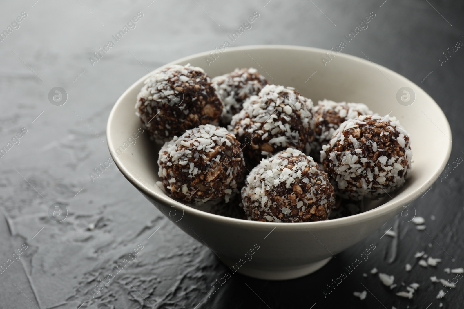 Tasty chocolate candies with nuts and coconut flakes in bowl on black table, closeup Photo of Tasty chocolate candies with nuts and coconut flakes in bowl on black table, closeup