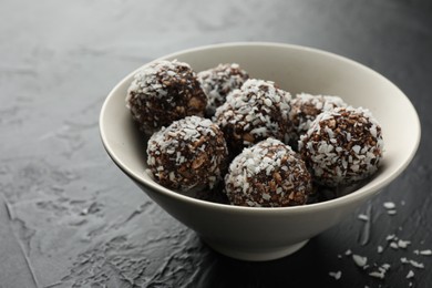 Photo of Tasty chocolate candies with nuts and coconut flakes in bowl on black table, closeup