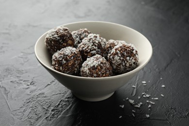 Photo of Tasty chocolate candies with nuts and coconut flakes in bowl on black table, closeup