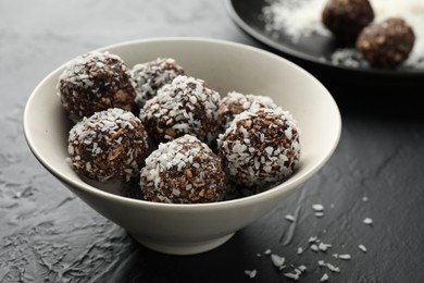 Photo of Tasty chocolate candies with nuts and coconut flakes in bowl on black table, closeup