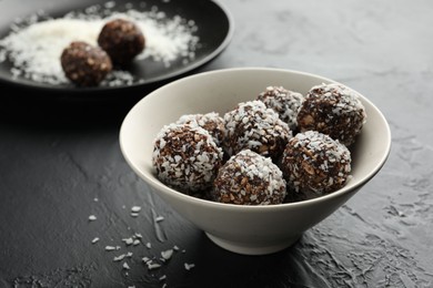 Photo of Tasty chocolate candies with nuts and coconut flakes in bowl on black table, closeup