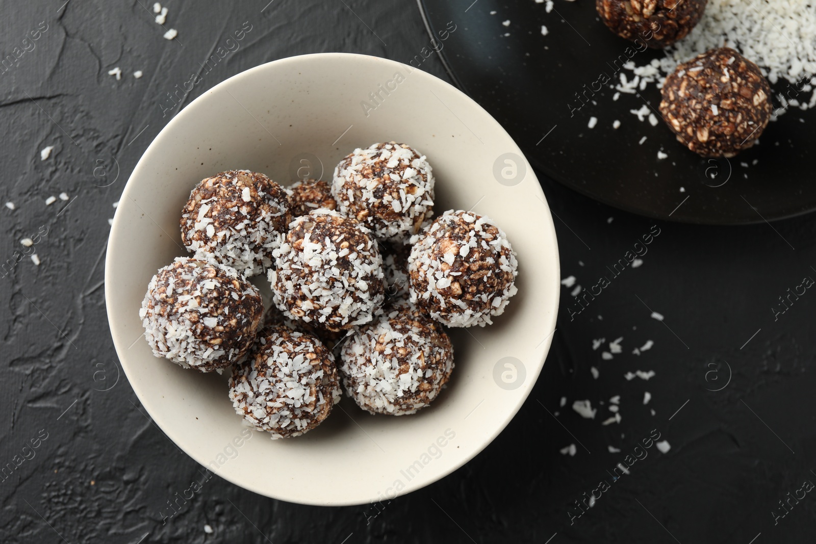 Tasty chocolate candies with nuts and coconut flakes in bowl on black table, flat lay Photo of Tasty chocolate candies with nuts and coconut flakes in bowl on black table, flat lay