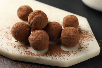 Photo of Tasty chocolate candies with cocoa powder on black table, closeup