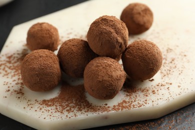 Photo of Tasty chocolate candies with cocoa powder on black table, closeup