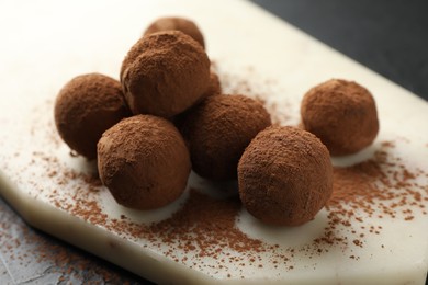 Photo of Tasty chocolate candies with cocoa powder on black table, closeup