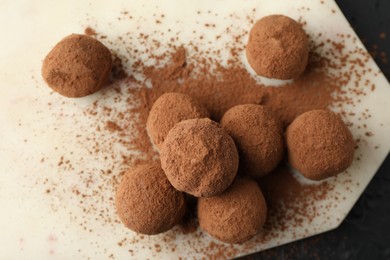 Photo of Tasty chocolate candies with cocoa powder on black table, top view